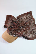 Overhead flat-lay of Knotycap's dark brown paisley bandana spread wide — white paisley motifs on chocolate base, beige corduroy brim at lower left